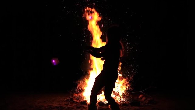 Girl is performing moves with her light poi's in front of a big camfire