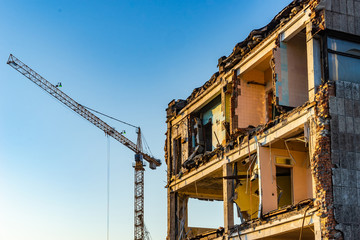 Demolition of houses. Half-demolished building. Construction of new houses. Destroyed building against the background of a construction crane.