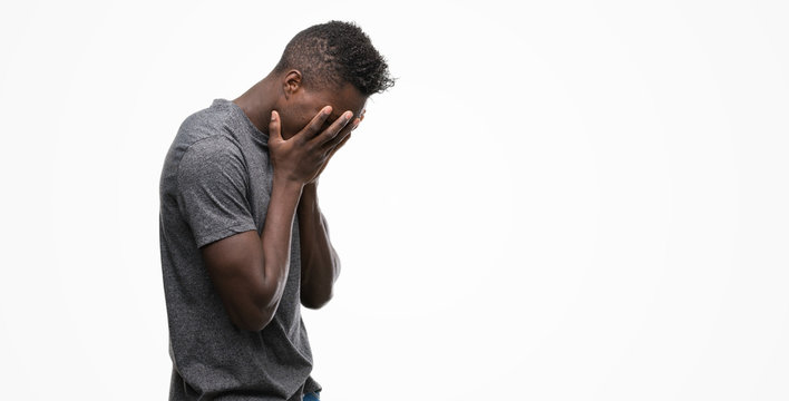 Young african american man wearing grey t-shirt with sad expression covering face with hands while crying. Depression concept.