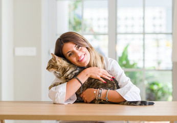Young woman at home playing with her cat with a happy face standing and smiling with a confident...