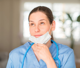 Young nurse woman wearing mask and stethoscope serious face thinking about question, very confused idea