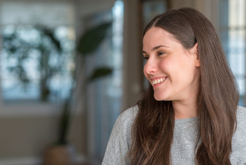 Fototapeta premium Young beautiful woman at home looking away to side with smile on face, natural expression. Laughing confident.
