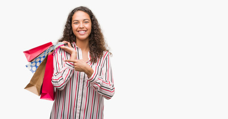 Young hispanic woman holding shopping bags very happy pointing with hand and finger