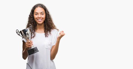 Young hispanic woman holding trophy screaming proud and celebrating victory and success very excited, cheering emotion