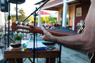 Musician playing guitar on a sunny terrace  with blurry people enjoying coffees in the background