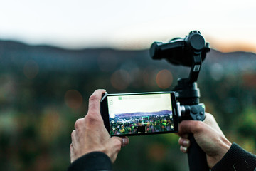 Man operating a gimble camera from a cellphone, seen from behind, with blurry nature background