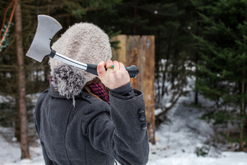 Girl dressed in winter clothes holds an axe in front of a wooden board as part of an axe throwing...