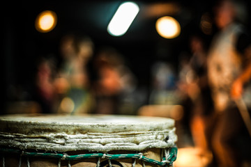 Close up of a djembe skin, with blurry drummers in the background