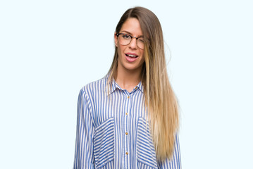 Beautiful young woman wearing elegant shirt and glasses winking looking at the camera with sexy...
