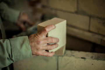 Brickmason's hand holding a brick in front of a brick wall