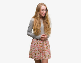 Blonde teenager woman wearing flowers skirt with hand on stomach because indigestion, painful illness feeling unwell. Ache concept.