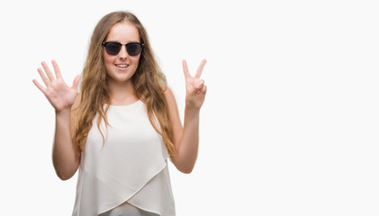 Young blonde woman wearing sunglasses showing and pointing up with fingers number seven while smiling confident and happy.