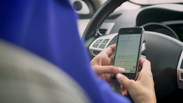 Back view of muslim woman typing on phone behind the self-driving steering wheel of an autonomous autopilot driverless car