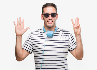 Handsome young man wearing headphones showing and pointing up with fingers number eight while...