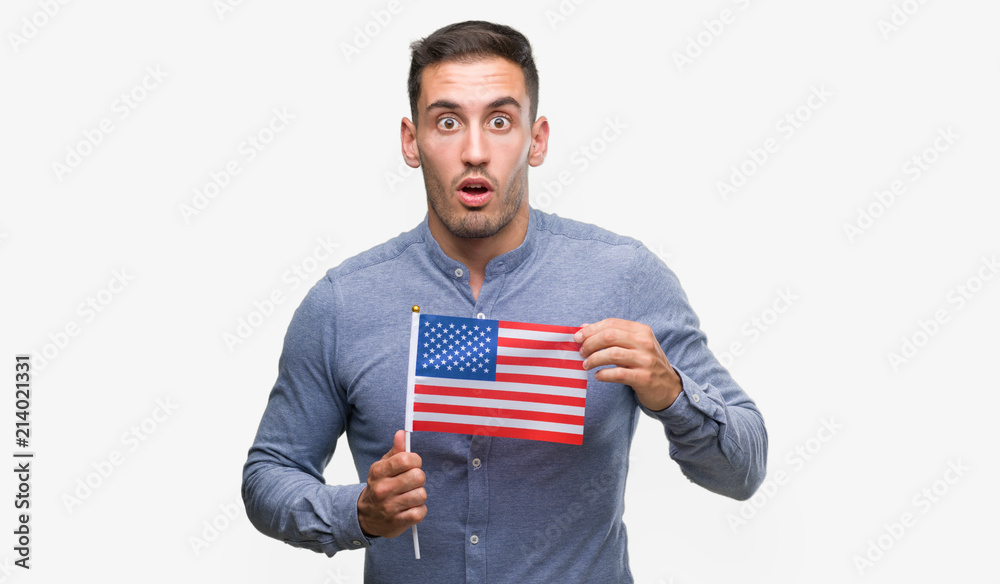 Poster Handsome young man holding a flag of America scared in shock with a surprise face, afraid and excited with fear expression