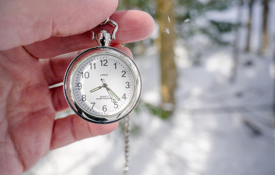 Pocket watch taken by thumb index and in hand in the forest in winter