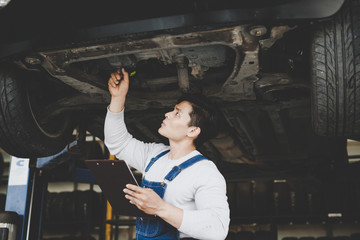 Asian young man mechanic holding clipboard checklist the car at service center. Repair...