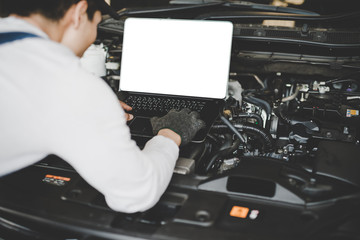 Young men mechanic working on a computer connected to a car engine. Mockup computer
