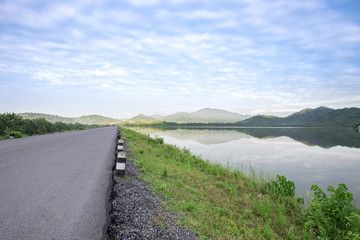 Fototapeta na wymiar Asphalt road with reservoir on clearly blue sky and mountains.