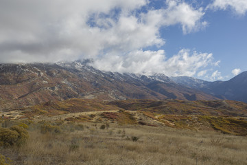 Panoramic view of mountains with short grass field upfront. Fall colors. Snow on top of mountains.