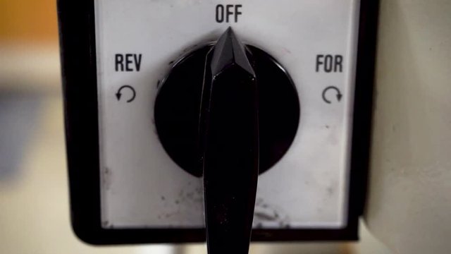 Close up footage of the power switch of a woodshop drill press being turned from Reverse to Off.