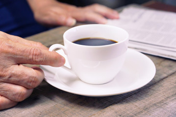 Hand grap white coffee cup on working table with background business man is reading newspaper.