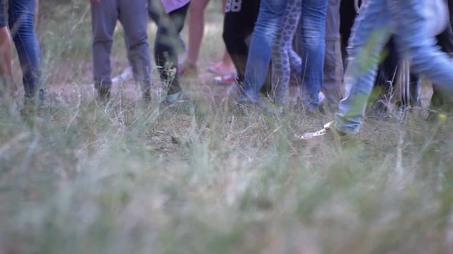 Legs of a crowd of people walking along the path in the woods in the evening. The camera moves with people. Close-up of Crowd feet. Many Legs of children walking in the forest