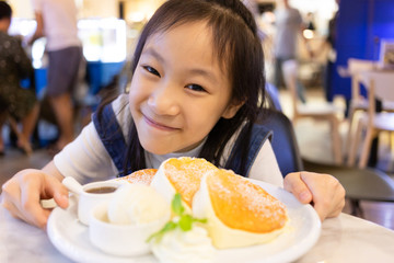 Attractive happy girl sitting and eat dessert,Close up portrait little girl eat panckaces in the restaurant