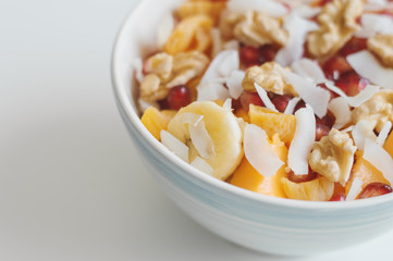 Salad bowl with banana, mango fruit, tangerine, coconut flakes, pomegranate seeds and walnut. Vegan food. Vitamins, carbs and fiber
