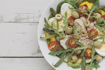 Fresh salad with eggs, canned tuna, sliced cherry tomatoes, arugula, cucumber, spinach, green beans, yellow bell pepper and olives on wooden table, top view. Portion of healthy meal