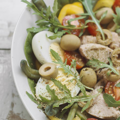 Square photo of Nicoise salad with tuna, boiled chicken eggs, arugula, spinach, cucumber, tomatoes, green beans, pepper and olives