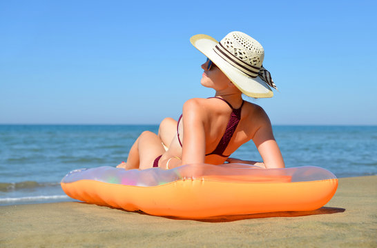 Caucasian girl with hat lying on inflatable mattress on the beach. Summer vacation by the sea.
