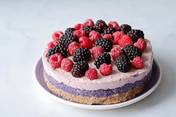 Raw vegan cake with raspberries and bluberries on white table