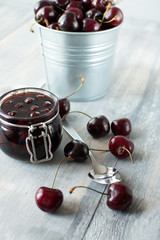 cherry marmalade in a glass jar with a lid, a jar stands in red cherries, conservation for the winter. selective focus and copy space