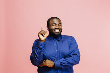 Portrait of a smiling man in blue shirt pointing up, isolated on pink background