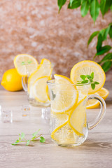 Refreshing mineral water with lemon, mint and ice cubes in glasses on a wooden table
