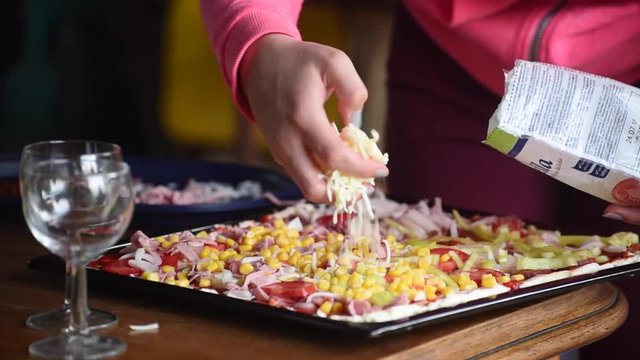 Closeup of girls hands sprinking cheese on pizza