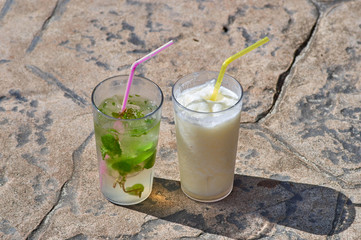 Two glasses with different cocktails stand on stone slabs on a s
