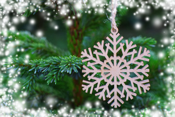 Wooden snowflake on christmas tree as winter holiday decoration with white illustrated snowflakes along edges of image.  Merry christmas and happy new year greeting card.