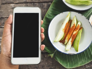 Smart phone on hand and tropical mango