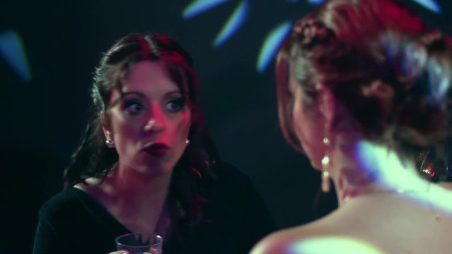 Close up of a woman arguing and complaining to a female friend in a night club while drinking wine