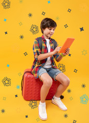 Wonderful tablet. Positive curious boy sitting on his luggage and playing games in his tablet
