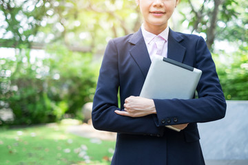 Young businesswoman holding tablet PC at outdoors. Front view image with copy space.