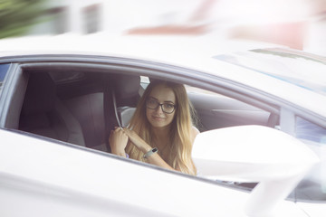 smiling, beautiful girl blond in glasses with an expensive white car on the road is standing