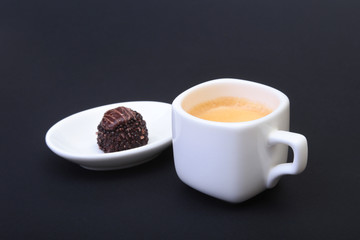 White cup of classic espresso coffee and pralines on black background.