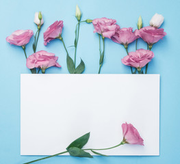 Flowers composition. Wreath made of pink flowers with white paper card on blue background. Flat lay, top view, copy space