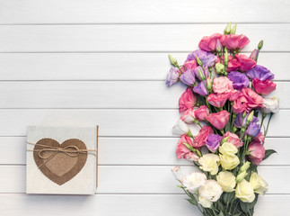 Beautiful bouquet of pink, purple, yellow eustoma flowers and handmade gift box on white wooden background. Copy space, top view,