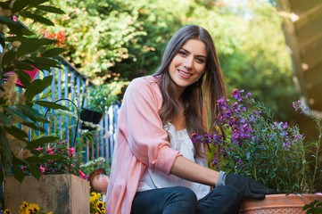 Pretty young girl smiling and gardening in pots on the terrace,at home, with working gloves....