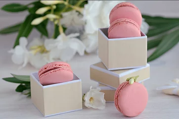 Gordijnen Roze frambozen macarons in de geschenkdoos op houten achtergrond. Franse dessertmakarons en witte bloemen voor het beste cadeau of verrassing. © vasanty