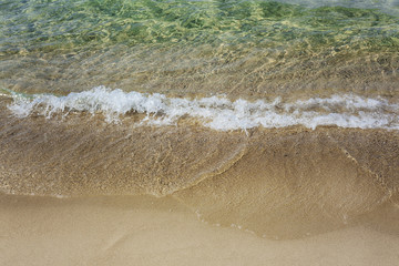 Sand beach with emerald blue water and wave foam
